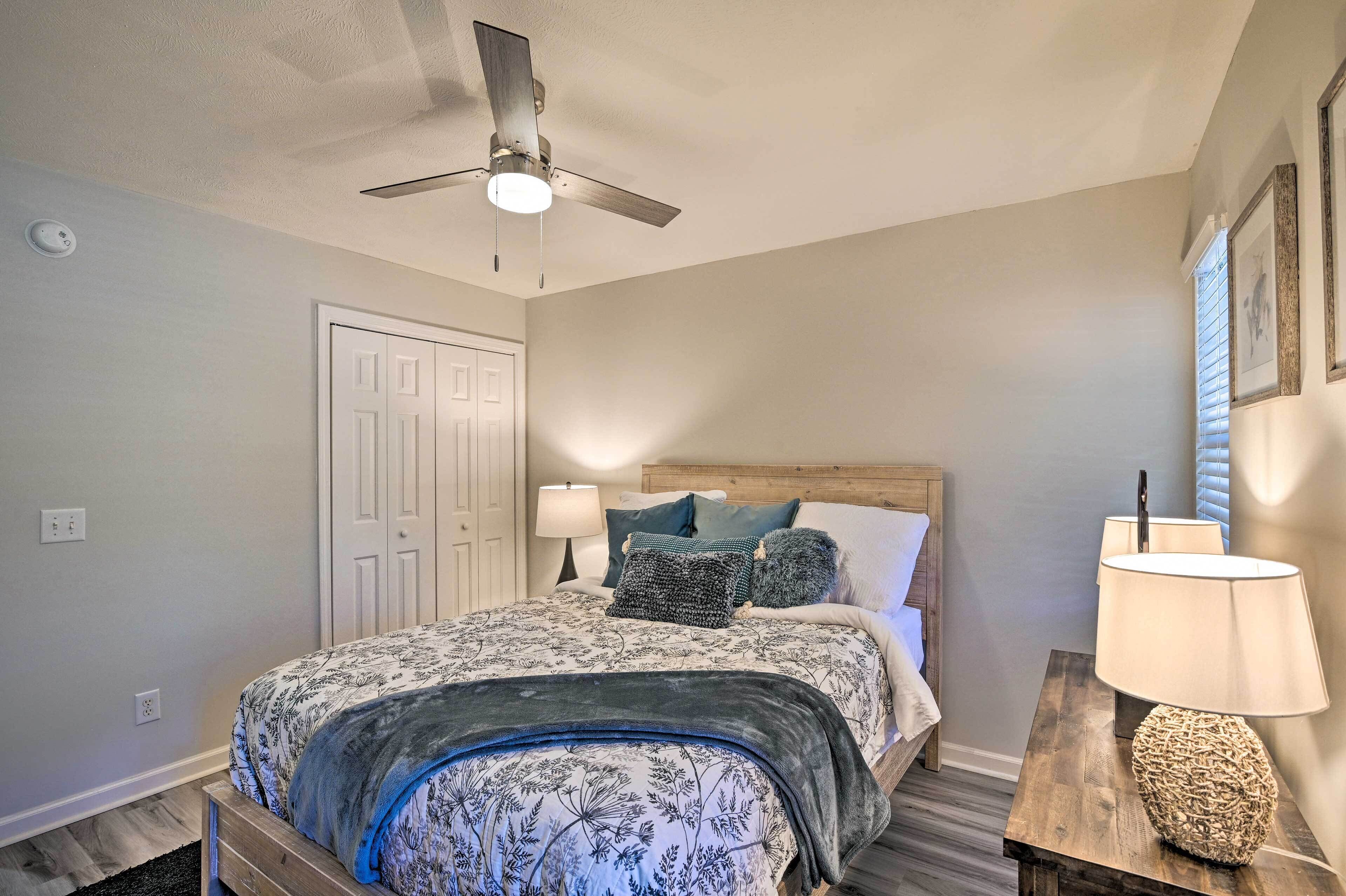 A bedroom with a bed, a ceiling fan, a nightstand with a lamp, and a door.