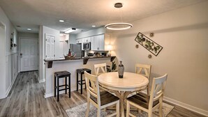 A modern kitchen with white cabinets, a central island, and a dining area with a round table and wooden chairs. - Welcome to ‘After Dune Delight’ Golf Course Condo! (Pawleys Island)