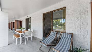 A modern interior with a dining area, two striped lounge chairs, and a large window with a view.