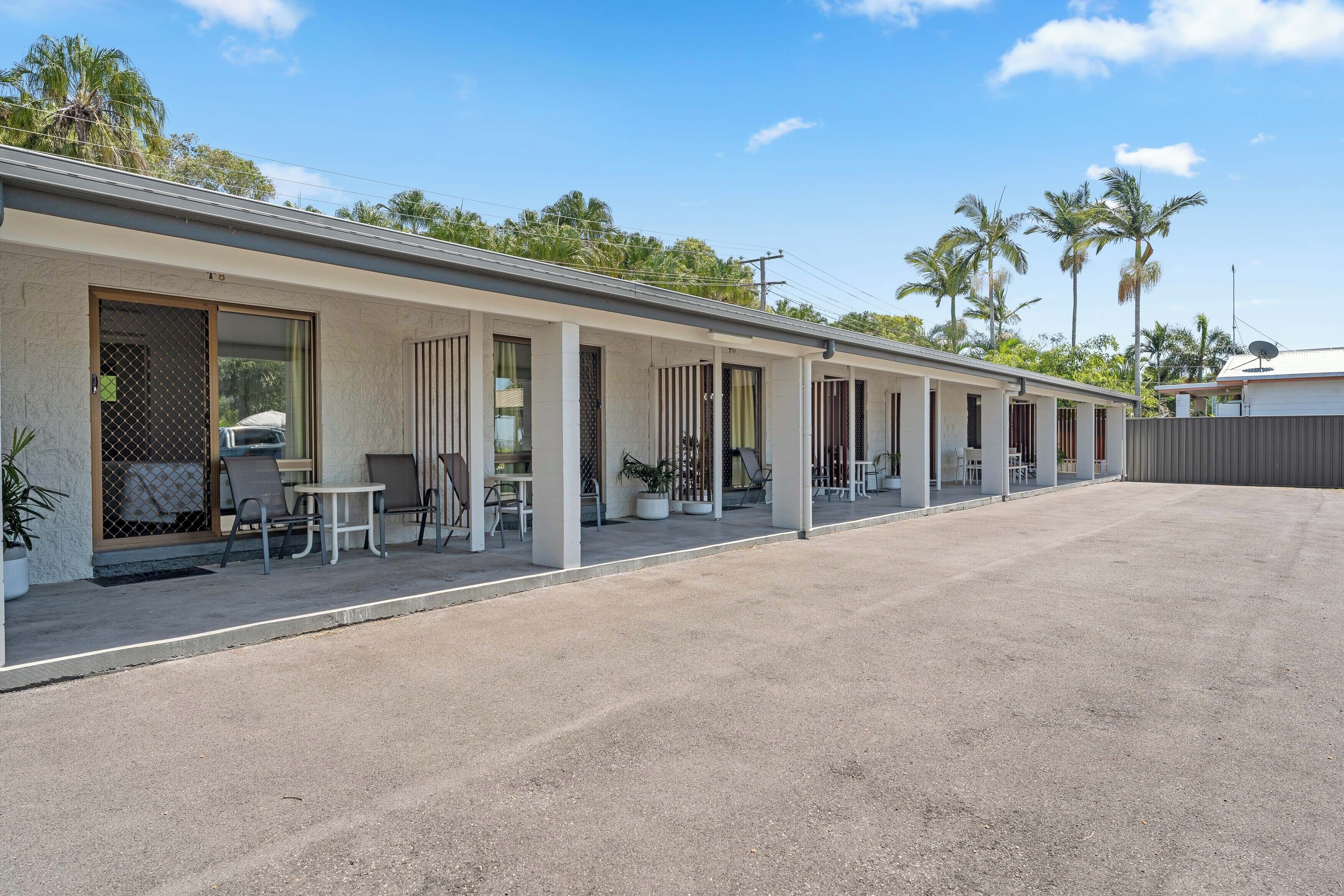 Un motel avec une rangée de chambres, des places assises à l’extérieur et des palmiers en arrière-plan.