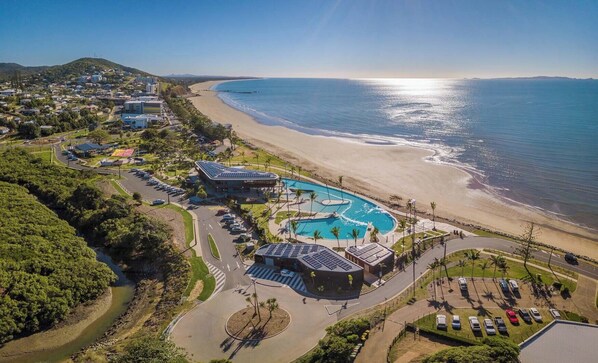 Vista aérea de un complejo turístico en la costa, con piscina, playa y vegetación circundante.
