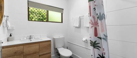 A bathroom with a white sink, wooden vanity, toilet, and a shower curtain with a leaf pattern.