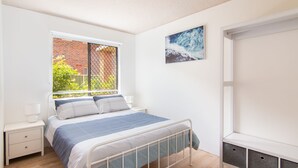Une chambre à coucher comprenant un lit, une table de chevet, une fenêtre donnant sur un mur de briques et de la verdure, et un tableau accroché au mur.