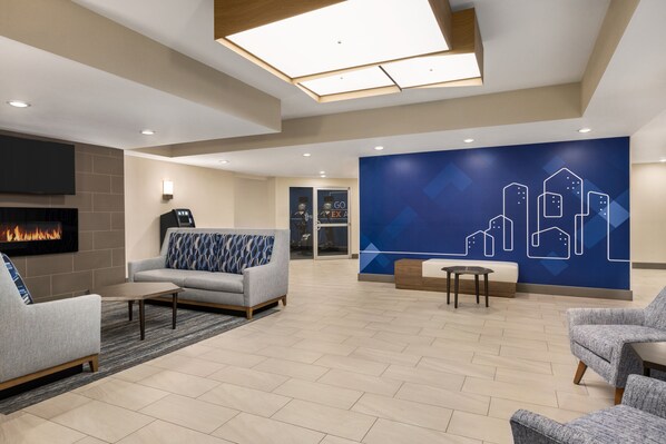 Een moderne lobby met een open haard, een zithoek en een muur met een geometrisch stadsgezicht.