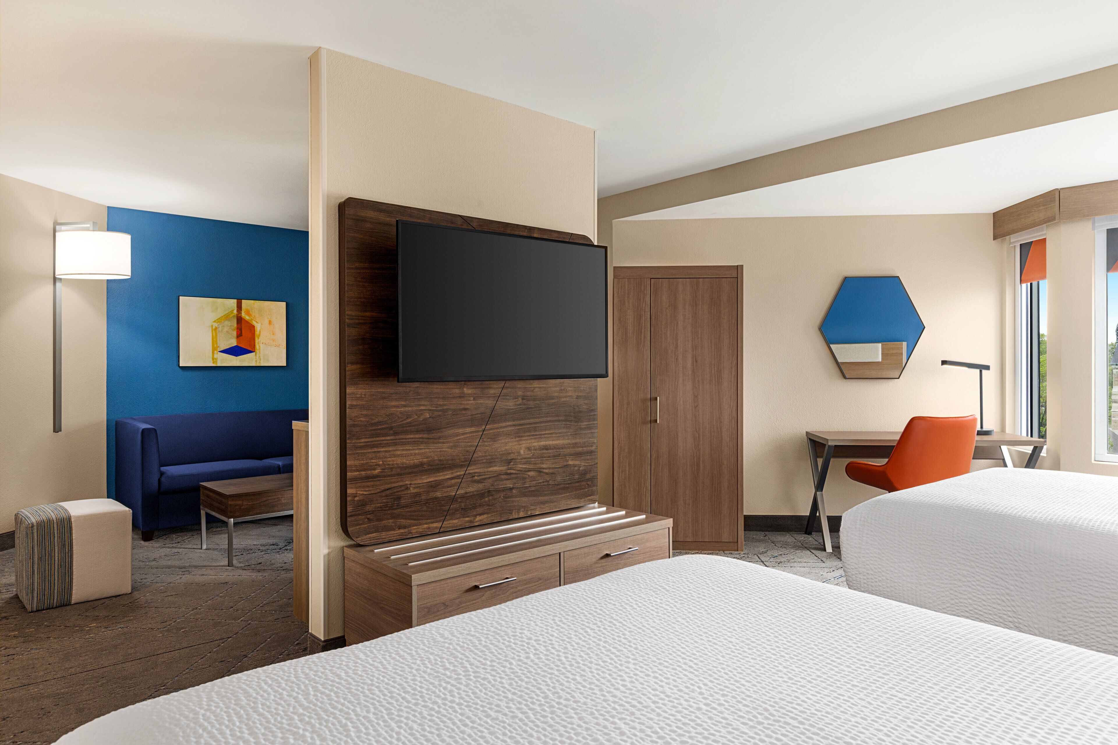 A hotel room with two beds, a desk, a chair, a TV, and a sofa.