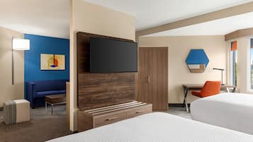 A hotel room with two beds, a desk, a chair, a TV, and a sofa.