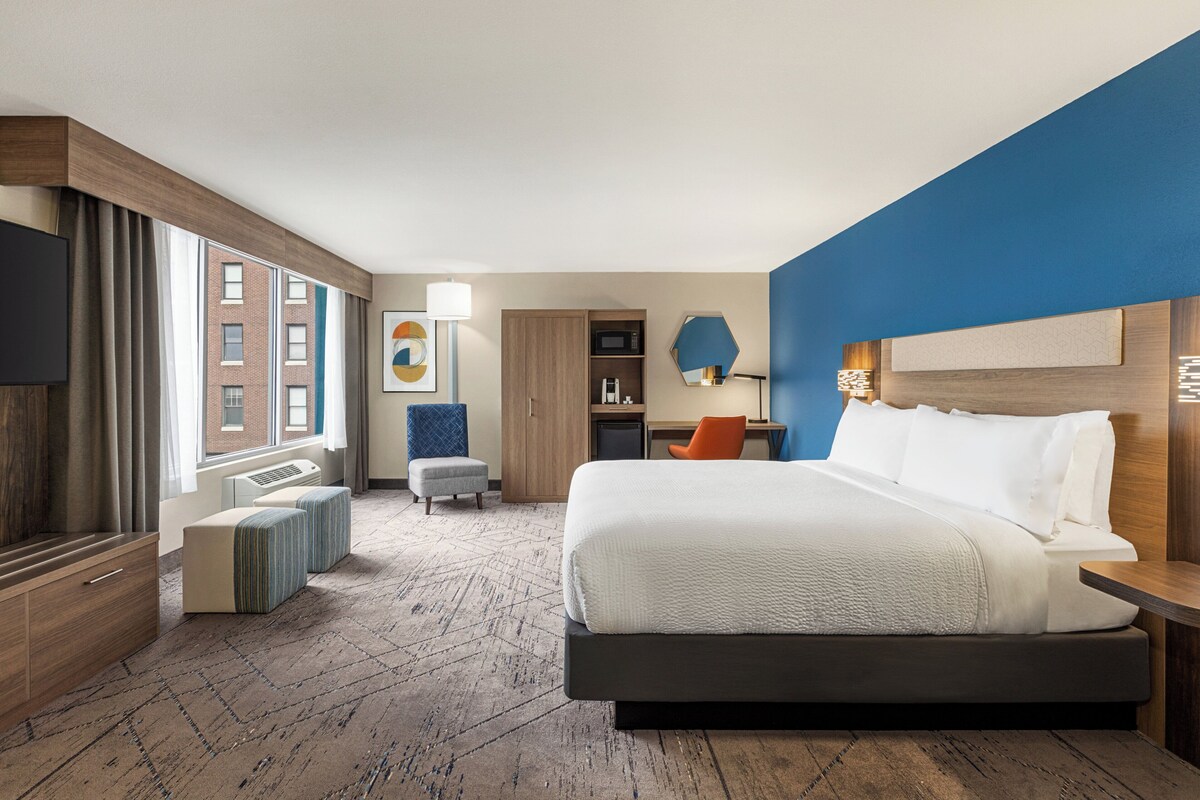Une chambre d’hôtel avec un grand lit, un bureau, une chaise et un téléviseur.