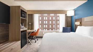 A hotel room with a bed, a desk, a chair, a television, a microwave, and a window with a view of a building.