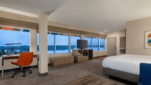 Une chambre d’hôtel moderne dotée d’un grand lit, d’un bureau avec un ordinateur, d’une télévision et offrant une vue sur un lac.
