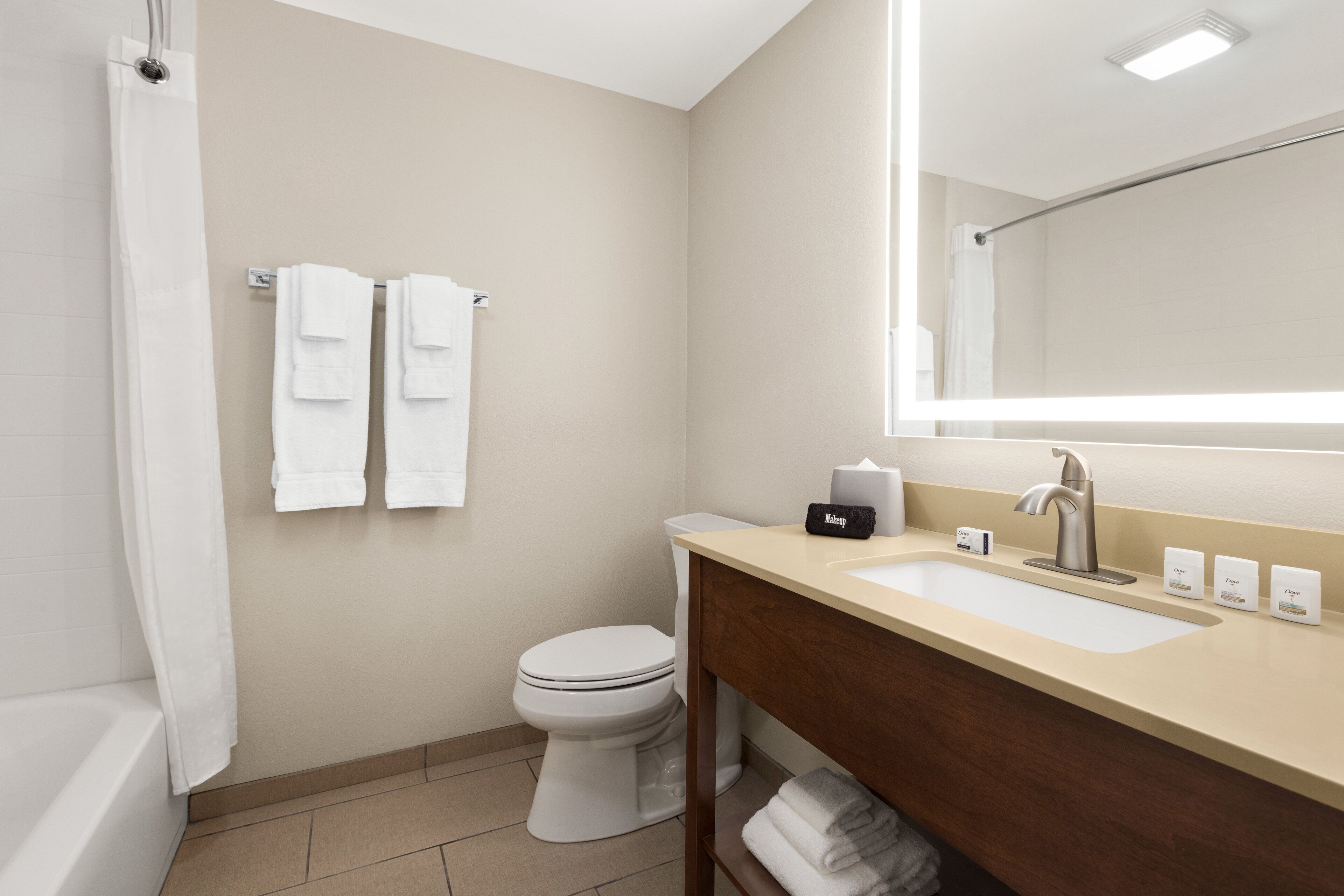 A modern bathroom with a toilet, sink, and mirror. There are two towels hanging on the wall and a shower curtain.