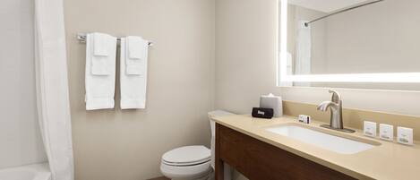 A modern bathroom with a toilet, sink, and mirror. There are two towels hanging on the wall and a shower curtain.
