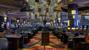 Un casino doté de nombreuses tables de jeux et de machines à sous, d’une moquette aux couleurs vives et d’un lustre.
