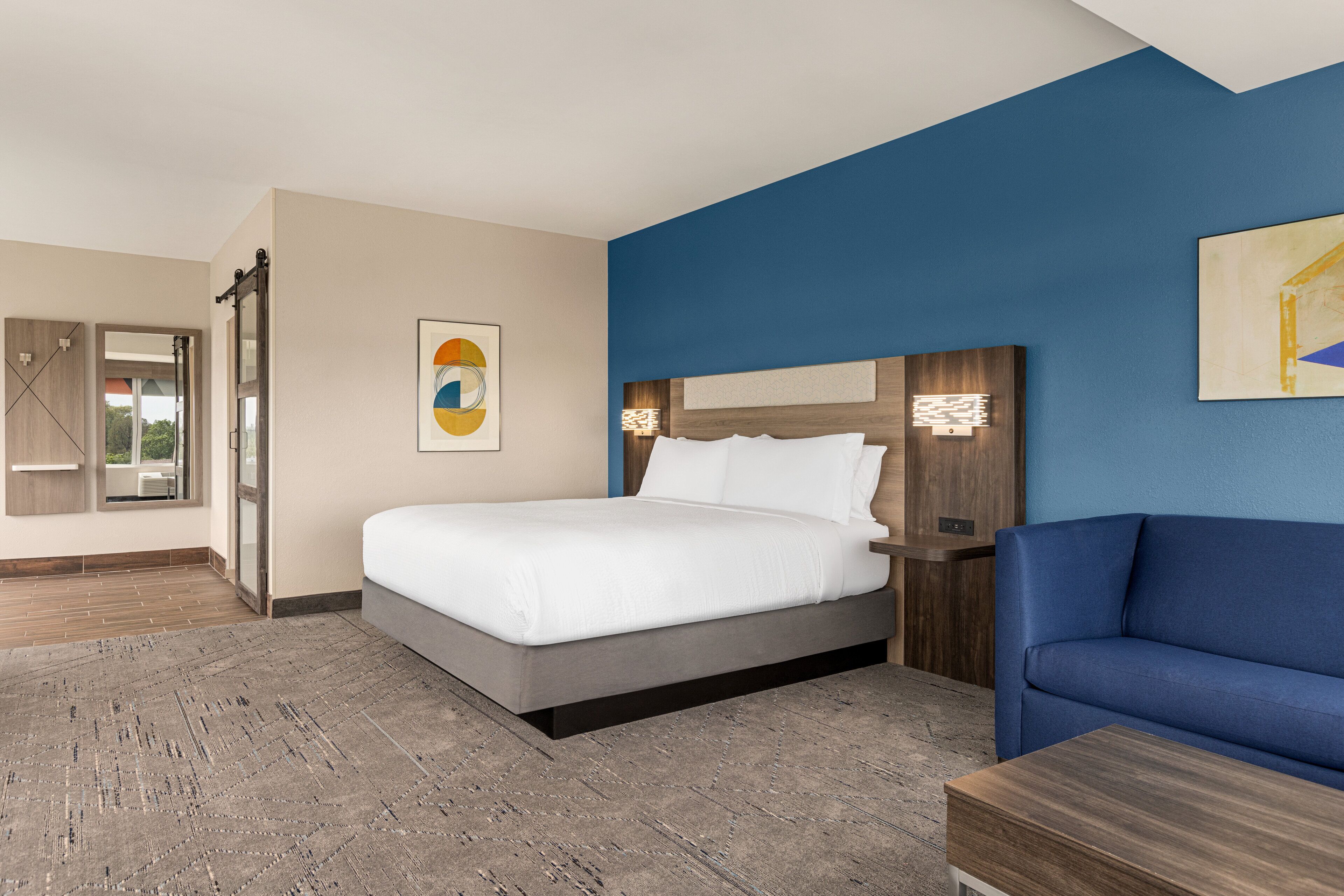A hotel room with a bed, a blue sofa, a nightstand, and a large window.
