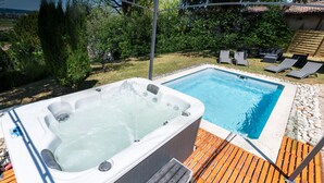 A hot tub and a swimming pool on a wooden deck with lounge chairs.