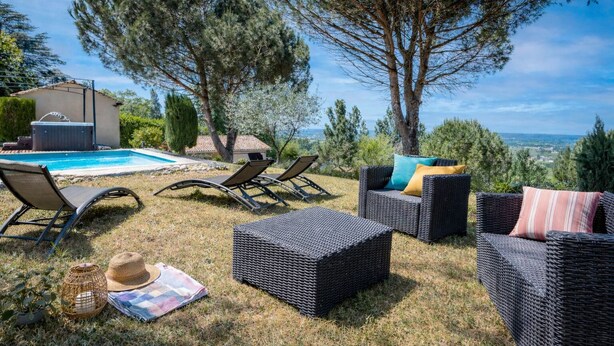 A poolside area with lounge chairs, a hot tub, and a view of the landscape.