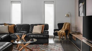 Ett modernt vardagsrum med en svart lädersoffa, ett soffbord i glas, en mönstrad matta och en stor TV med platt skärm.