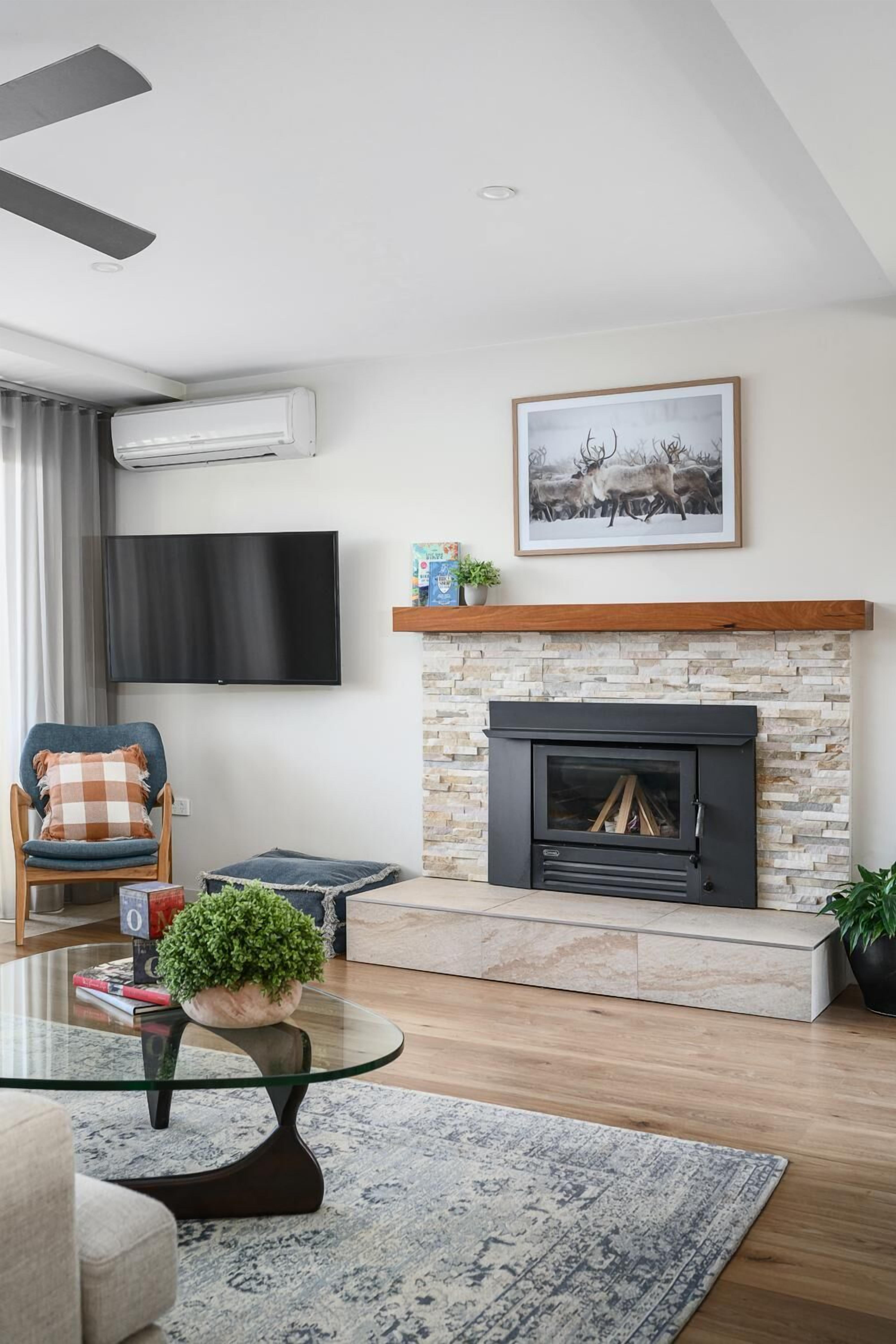 A modern living room with a fireplace, a flat-screen TV, a comfortable chair, and a glass coffee table.