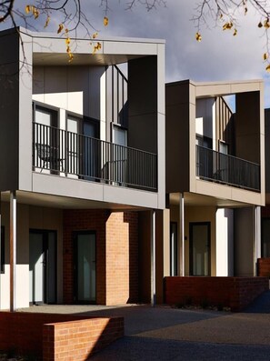 A modern multi-story residential building with balconies, brickwork, and large windows.