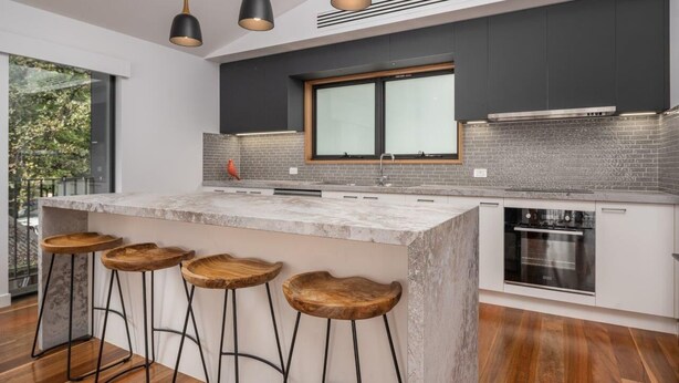 Una cocina moderna con una isla grande, taburetes de bar, luces colgantes y vistas al exterior.