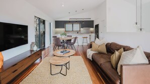 Una sala de estar moderna con un televisor grande, muebles de madera, un comedor con sillas y un ventilador de techo.