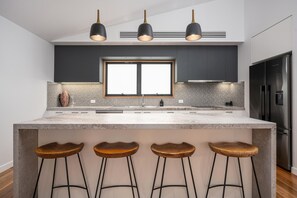 Une cuisine moderne dotée d’un grand îlot central, de tabourets de bar, de luminaires suspendus et d’un réfrigérateur en acier inoxydable.