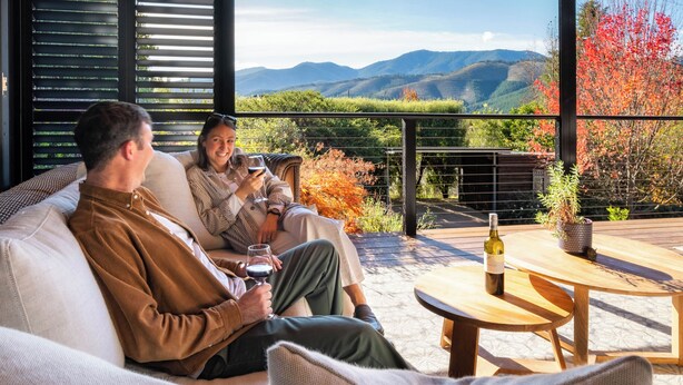 A couple relaxing on a sofa with a scenic view of mountains and autumn foliage. - 25 Walkers Lane - Luxurious living with breath taking views (Bright)