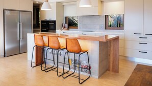 A modern kitchen with a central island, bar stools, a stainless steel refrigerator, and a large window with a view. - 25 Walkers Lane - Luxurious living with breath taking views (Bright)