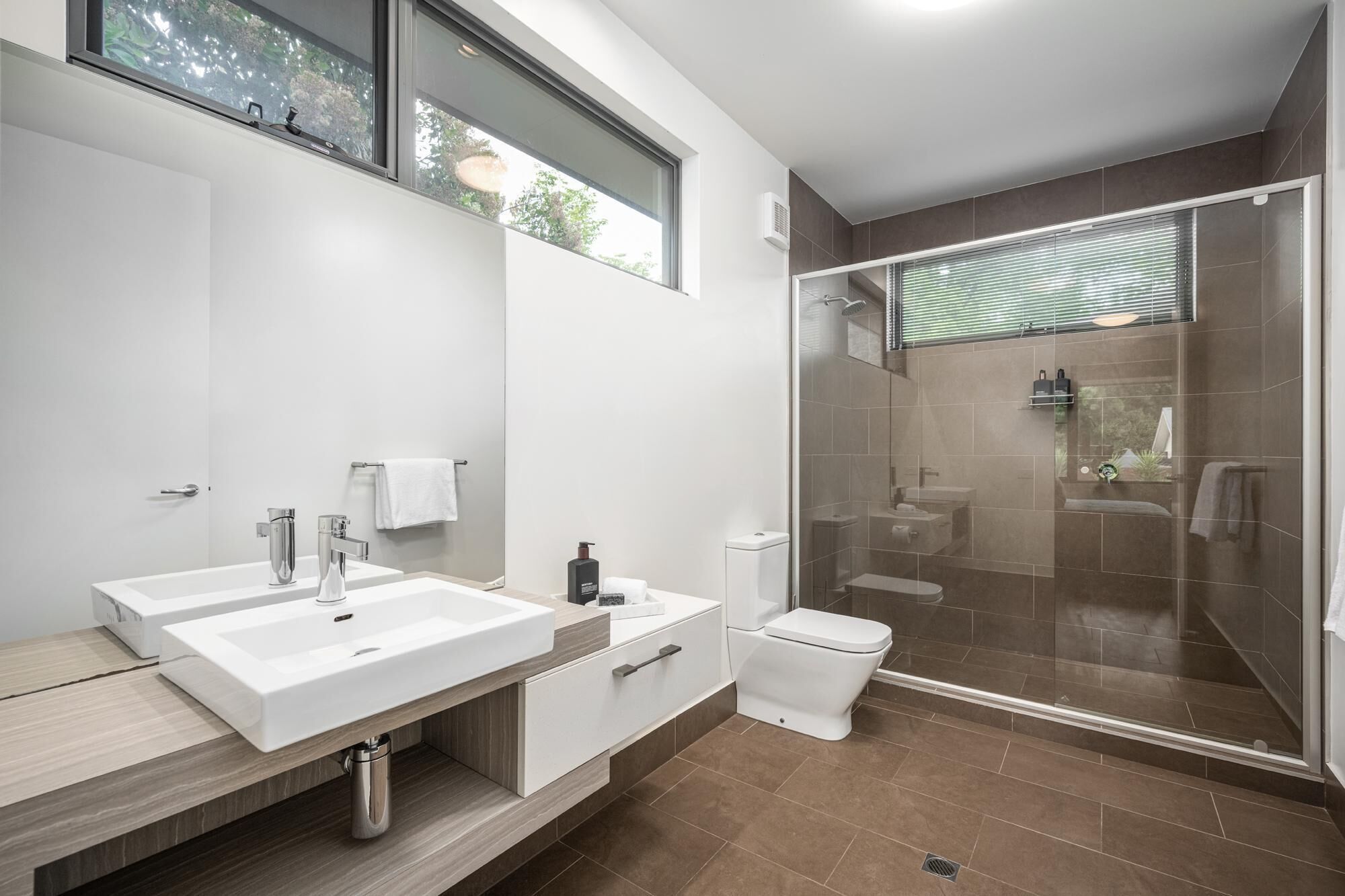 A modern bathroom with two sinks, a toilet, and a glass-enclosed shower area.