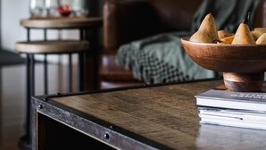A cozy living room with a wooden coffee table, a bowl of pears, and a bookshelf.