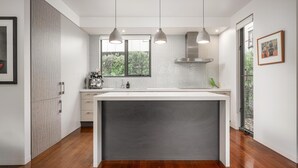 A modern kitchen with a central island, pendant lighting, and a view of greenery outside.