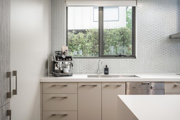 Una cocina moderna con cafetera, un lavamanos y una ventana con vista a zonas verdes.