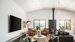 A spacious living room with a fireplace, leather sofas, and a large TV. - The Grove Estate - The pièce de resistance of this property is the view, be it the 360-degree views of the surrounding bush side, valley and the Region’s famous Mt Buffalo or perhaps the view of the spectacular and famous artwork showcased through th (Porepunkah)