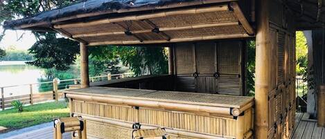 Una struttura in bambù con tetto di paglia, un pontile in legno e vista su un lago.