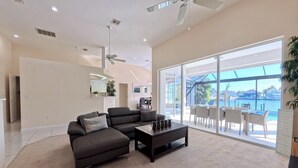 Ein geräumiges Wohnzimmer mit einem dunklen Sofa, einem Couchtisch und einer großen Schiebeglastür, die auf einen Balkon mit Blick auf das Wasser führt.