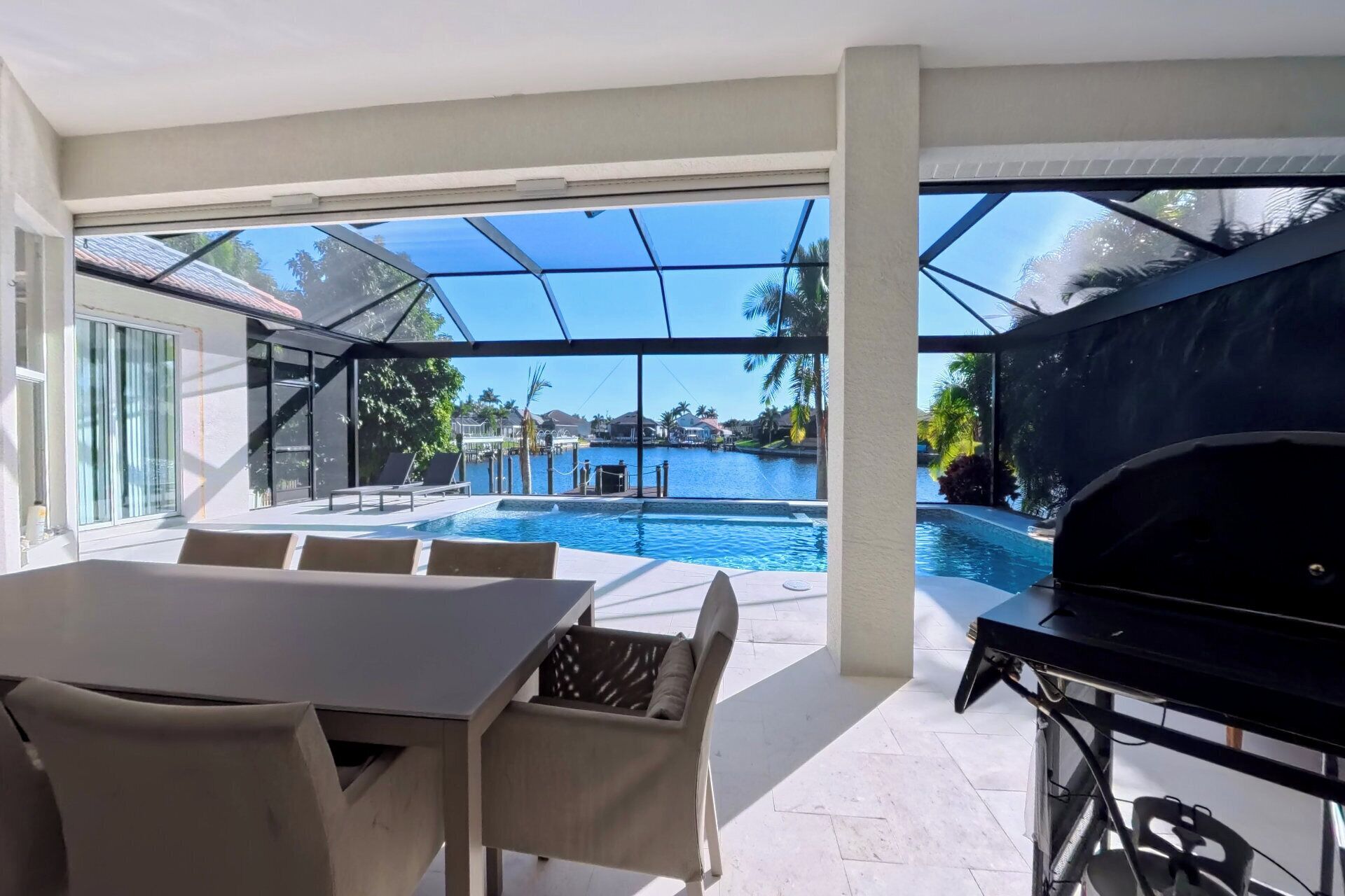 A modern outdoor patio with a pool, a dining area, and a barbecue grill.