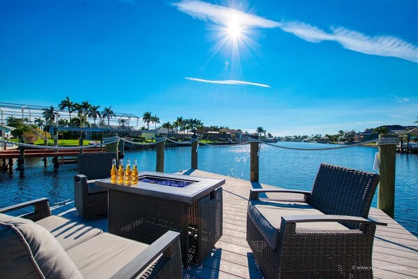 Relax on the waterfront deck with a table and two chairs, surrounded by palm trees and a residential area.