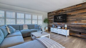 Una sala de estar moderna con un sofá modular, una mesa de centro y una pared de madera decorativa con un letrero de alquiler vacacional.