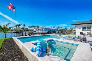 Relax by the pool surrounded by a lush garden and palm trees, with a dock offering access to water activities.