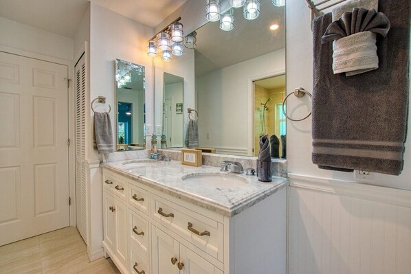 Un baño con dos lavamanos, un mueble de tocador con cajones, un perchero para toallas y un espejo con iluminación.