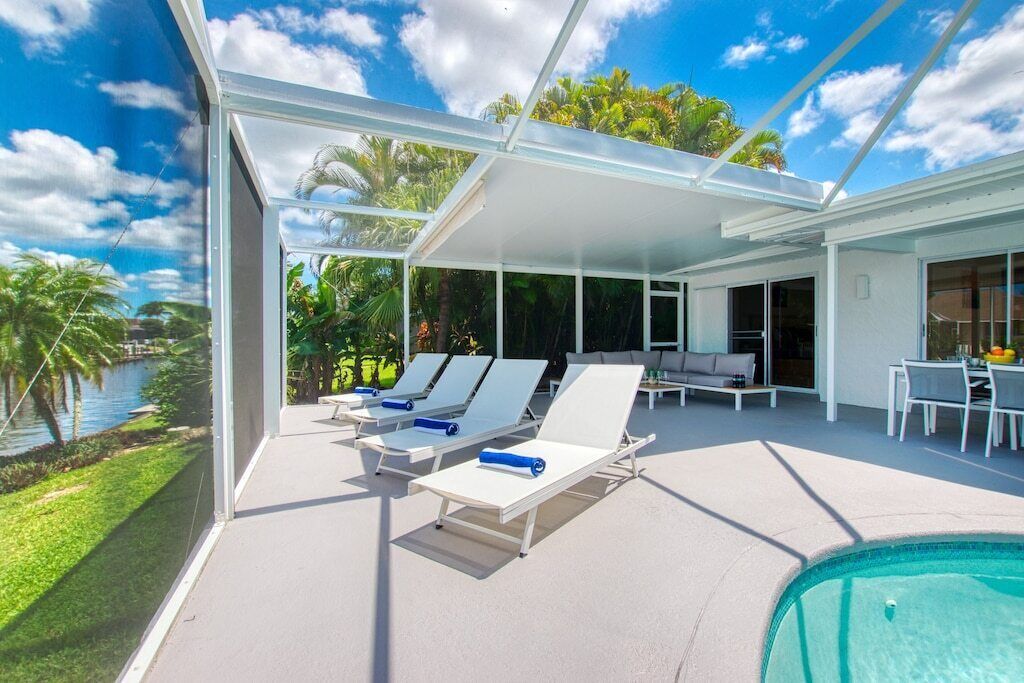 A poolside area with sun loungers, a covered seating area, and a view of a lake.