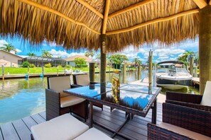 Un área de piscina al aire libre con techo de paja, sillas de descanso y una mesa de vidrio.