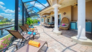 Un patio techado al aire libre con sillones de descanso, un comedor y vistas a una masa de agua.
