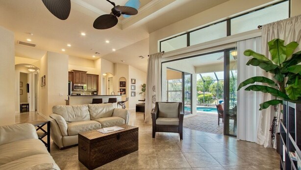 A spacious living area with a sofa, a coffee table, and a chair. There is a kitchen in the background, and a large sliding glass door leads to an outdoor area with a pool. - VRCC Villa Belle Mer (Cape Coral)