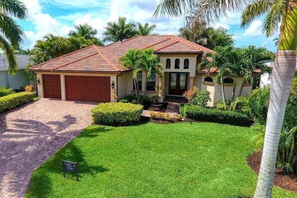 A two-story house with a red-tiled roof, a garage, and a well-maintained lawn with palm trees.
