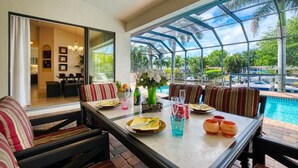 A dining area with a glass-enclosed patio overlooking a pool and lush greenery. - VRCC Villa Belle Mer (Cape Coral)