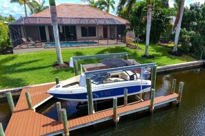 A boat docked at a wooden pier with a house in the background.