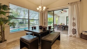 A spacious dining area with a large table, benches, and a view of a swimming pool. - VRCC Villa Belle Mer (Cape Coral)