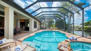 A covered swimming pool with lounge chairs and a bar area. - VRCC Villa Belle Mer (Cape Coral)