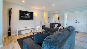 A modern living room with a grey sofa set, a glass coffee table, and a flat-screen TV mounted on the wall.