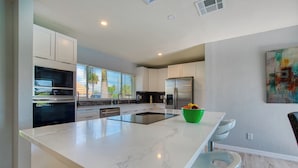A modern kitchen with white cabinets, stainless steel appliances, a marble countertop, and a green bowl on the island.